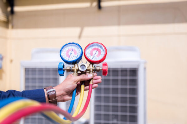 HVAC technician holding refrigerant gauge set with colorful hoses, demonstrating air conditioning maintenance and repair for Arizona homeowners.